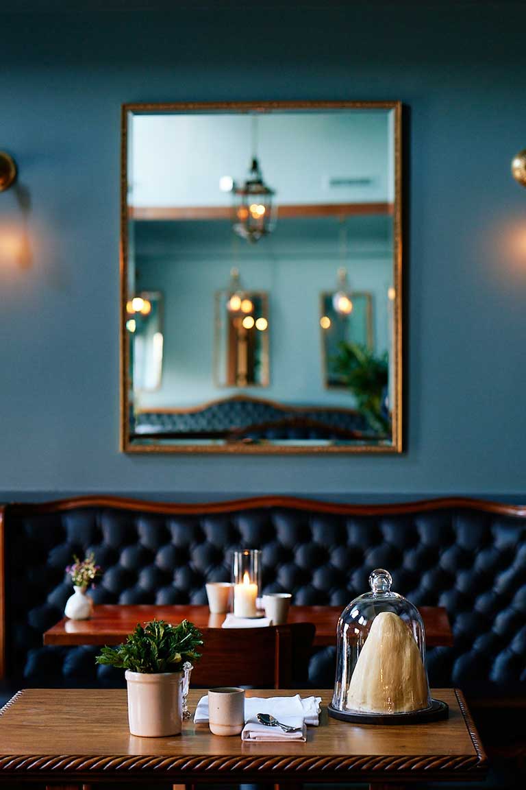 interior shot of manzke restaurant focused on the blue tufted banquette with a tablescape featuring a bell jar of butter and table settings in the foreground